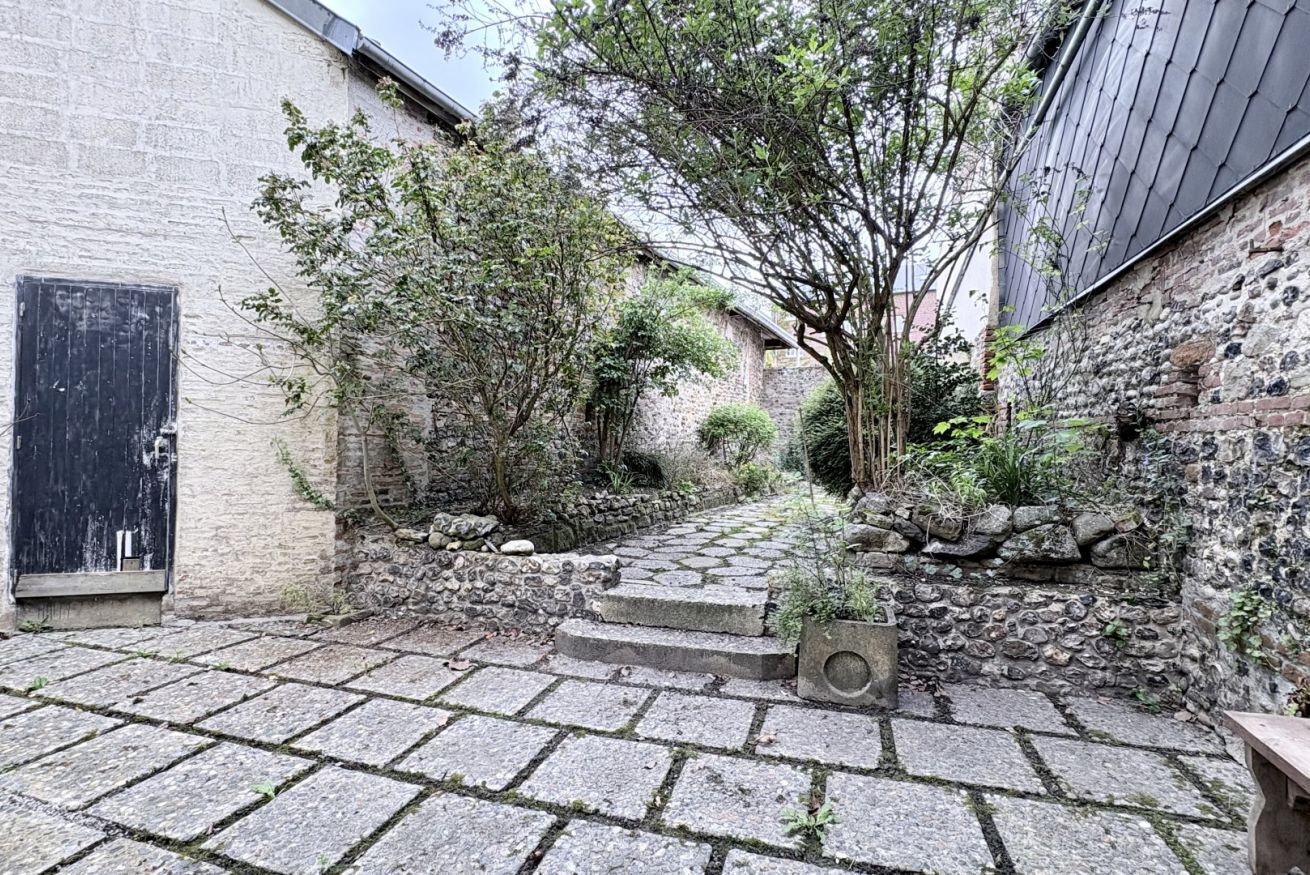 A stone pathway leading to a building with a black door, surrounded by greenery and stone walls.