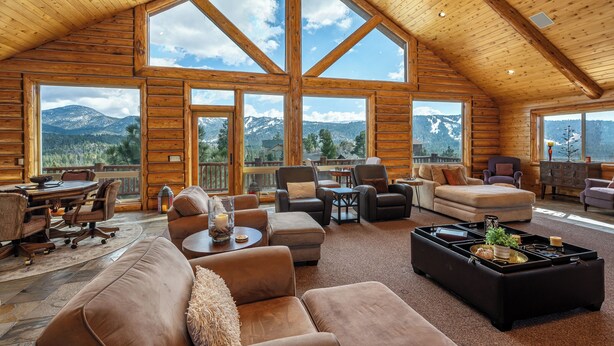 A spacious log cabin interior with large windows, a cozy seating area, and a dining table.