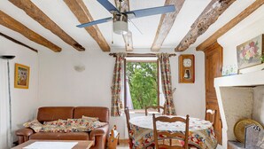 Ein Zimmer mit Holzbalkendecke, einem Esstisch mit Stühlen, einer Couch, einem Kamin und Blick durch ein Fenster.