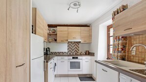Eine Küche mit Holzausstattung, Backofen, Geschirrspüler und einem Fenster mit gemusterten Vorhängen.