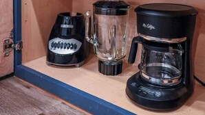 Keittiökaappi, jossa on kahvinkeitin, tehosekoitin ja vedenkeitin.