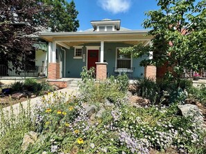 A house with a front porch, a brick chimney, and a garden with various plants and flowers. - Private Basement Studio - Near Wash Park (Denver)