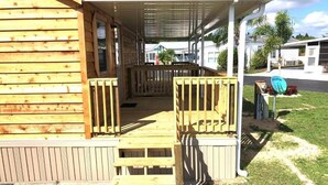 A wooden cabin with a porch, a covered outdoor area, and a small garden. - Woody's RV Resort (Sebring)