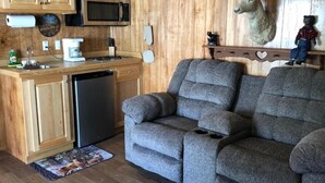 A compact living space with a kitchenette, a gray sofa, a mounted deer head, and a bear figurine. - Woody's RV Resort (Sebring)