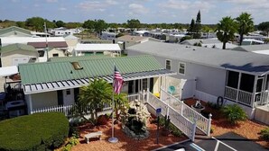 A row of mobile homes with a green roof, a white fence, and an American flag. - Woody's RV Resort (Sebring)