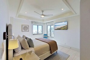A bedroom with a bed, a ceiling fan, a window with a view, and a wall-mounted TV. - Kiawah Exclusives | 5117 Windswept Villa (Kiawah Island)