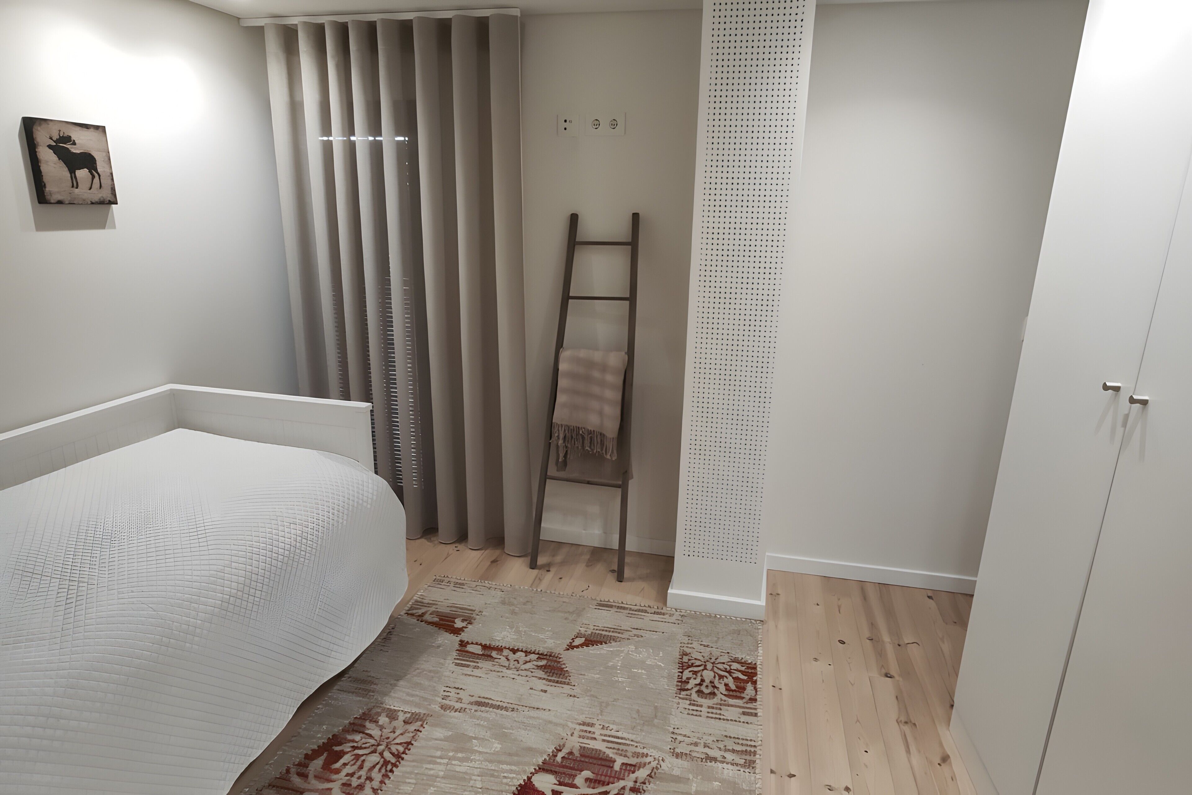 Une chambre à coucher avec un lit, une échelle en bois, un tapis à motifs et une œuvre d’art accrochée au mur.