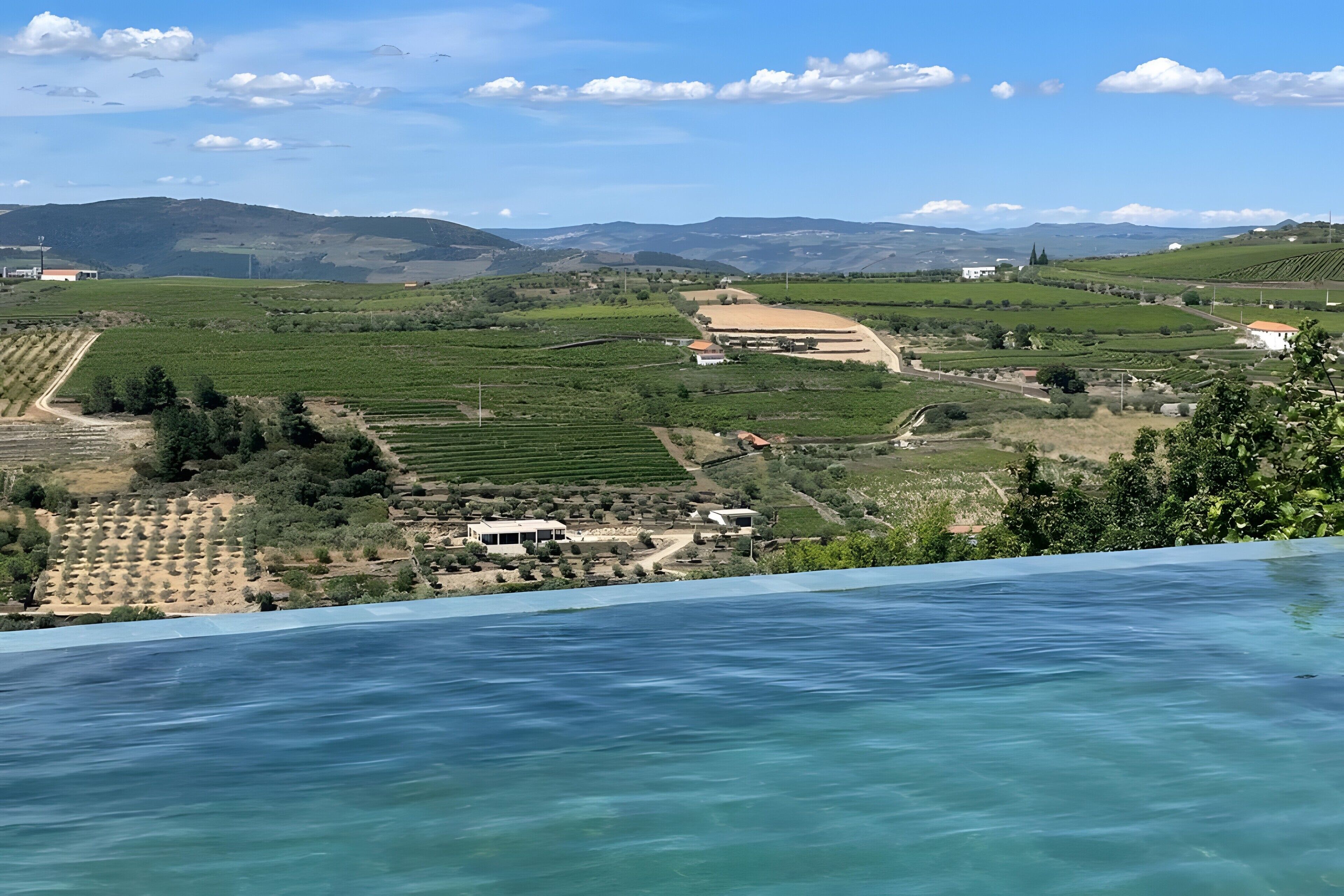 A coastal landscape with vineyards, a swimming pool, and distant mountains.