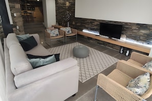 Una sala de estar moderna con un sofá, sillas, un televisor y una pared de piedra.