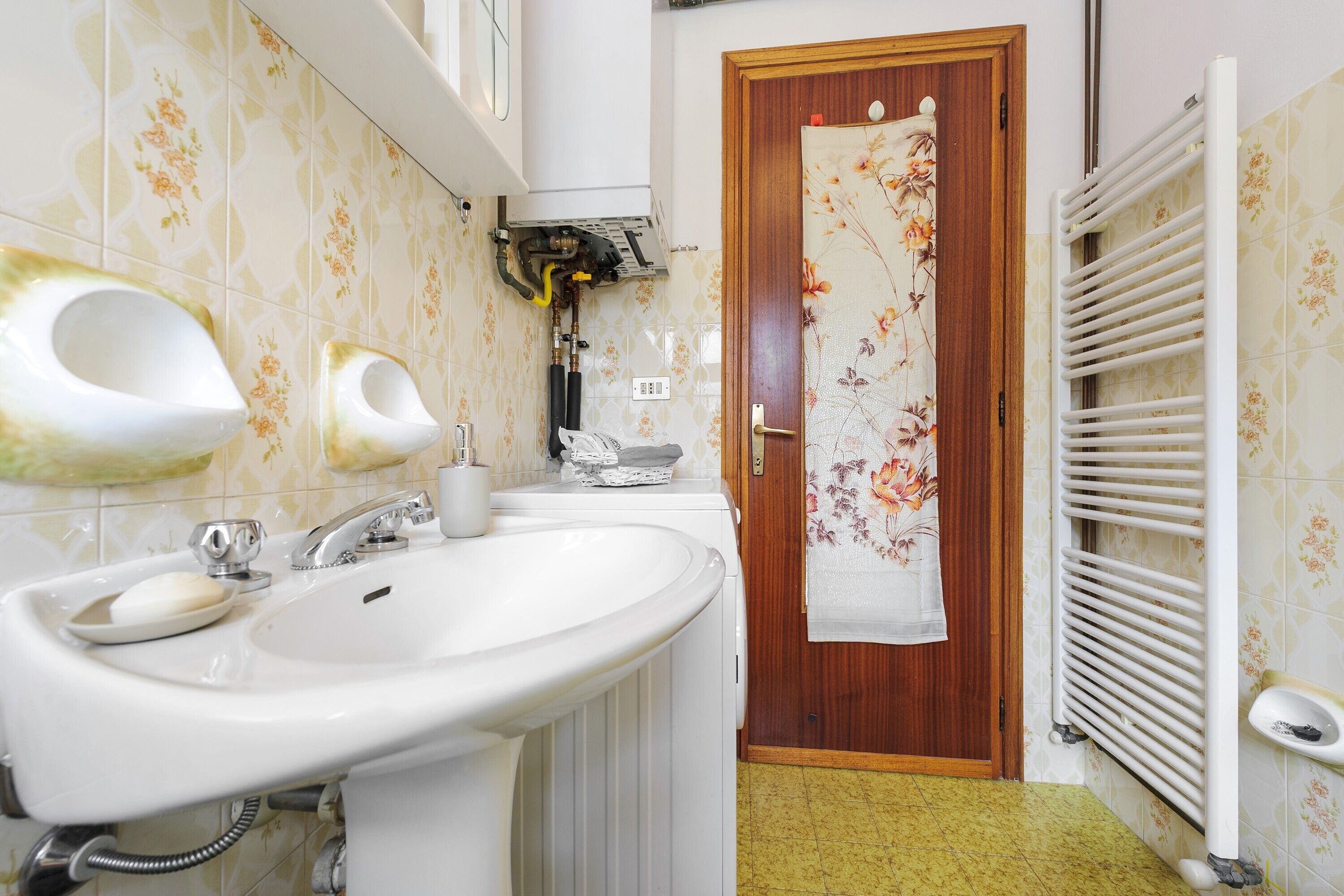 A bathroom with a sink, two urinals, a towel rack, and a radiator.