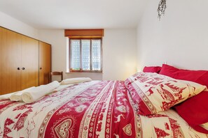 Un dormitorio con una cama, un armario de madera, una ventana con cortinas y una planta en la pared.