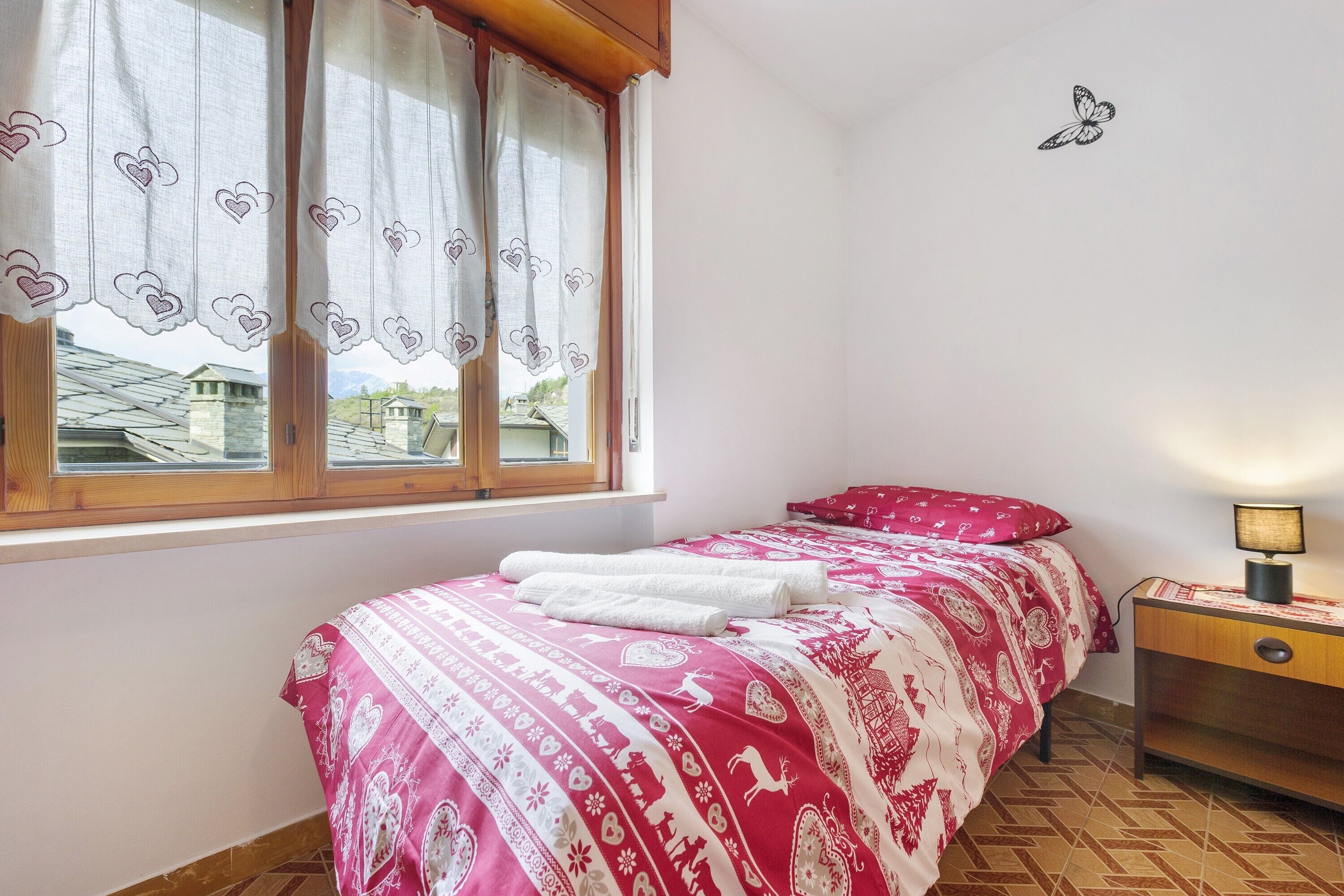 A bedroom with a bed, a nightstand, a lamp, a window with curtains, and a wall decoration.