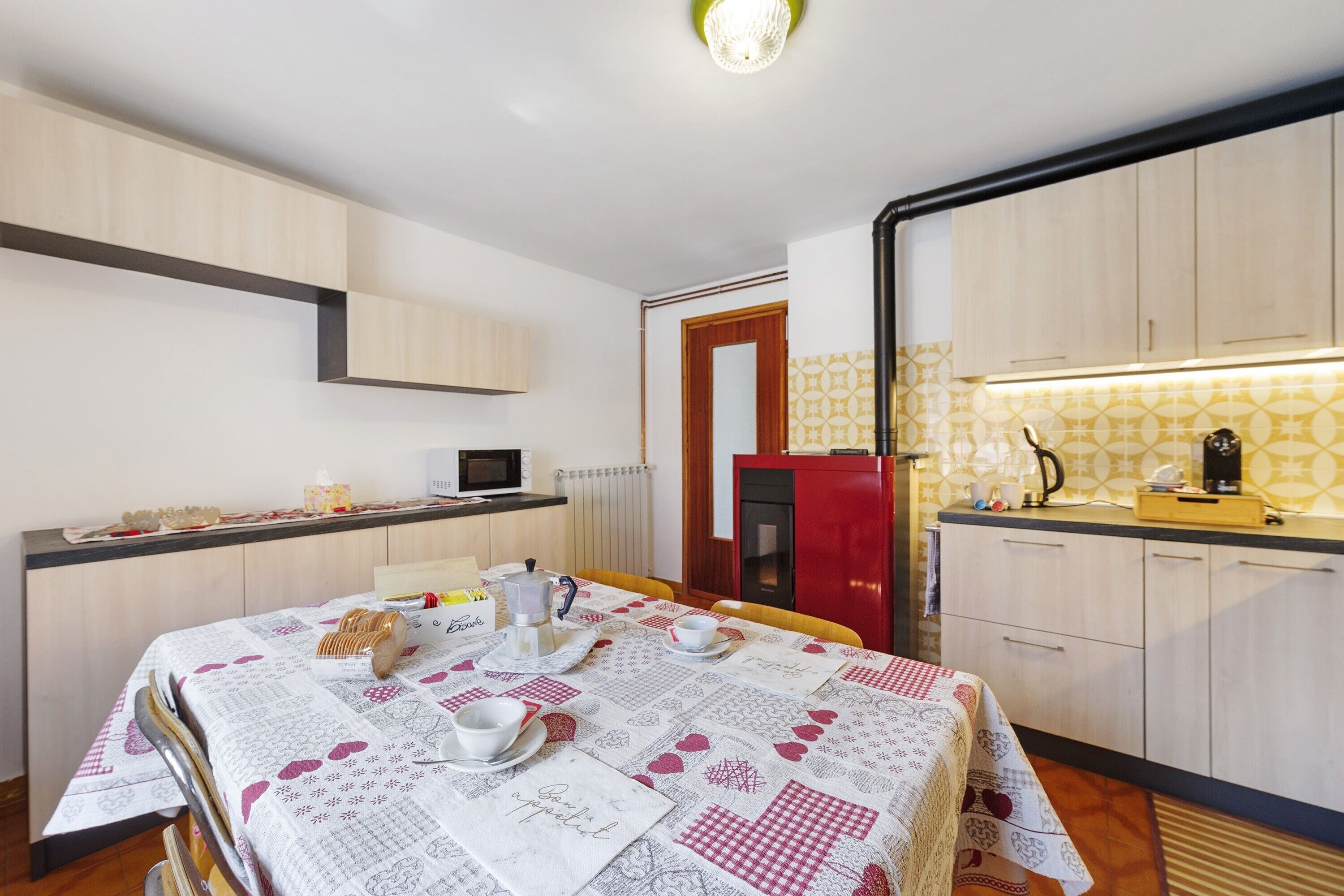 A compact kitchen with a dining table set for two, a red refrigerator, and a microwave.