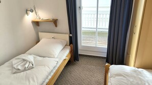 A single bed with a pillow and a folded towel, a bedside table with a lamp, and a window with curtains. - Villa Heimkehr Wohnung 10 by Interhome (Baabe)