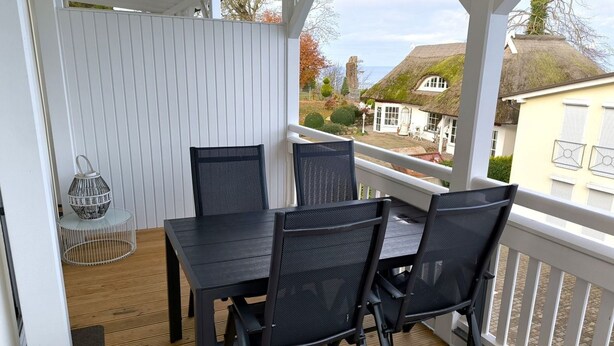 A covered outdoor seating area with a table and chairs, a lantern, and a view of houses and a windmill in the background. - Villa Heimkehr Wohnung 10 by Interhome (Baabe)