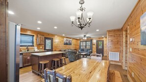 L’intérieur de la cabane est en bois et comprend une cuisine avec un évier et des placards, un coin repas avec une table et des chaises, ainsi qu’un ventilateur de plafond.