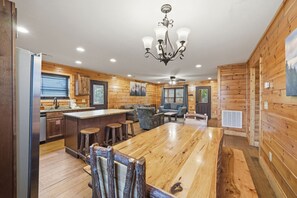 A cabin interior with a wooden interior, a kitchen with a sink and cabinets, a dining area with a table and chairs, and a ceiling fan. - Memory Maker Lodge:Hot Tub, Multicade, Grill, MORE (Gatlinburg)
