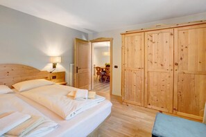 Habitación de hotel con cama, armario de madera, mesita de noche con lámpara y vista al comedor.