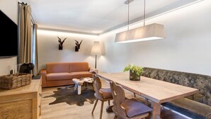 Ein modernes Wohnzimmer mit Esstisch aus Holz, einer Couch, einer Lampe und einem Fernseher.
