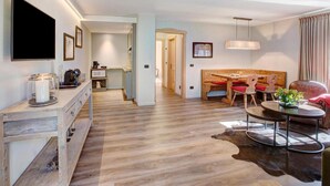 Ein modernes Wohnzimmer mit Holzboden, einem Essbereich mit roten Stühlen, einem an der Wand montierten Fernseher und einem großen Fenster.