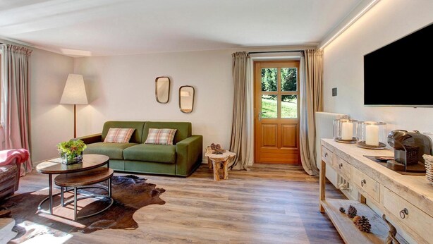 Ein Wohnzimmer mit einem grünen Sofa, einem runden Couchtisch, einer Lampe, einem Fernseher und einem Holzkasten.