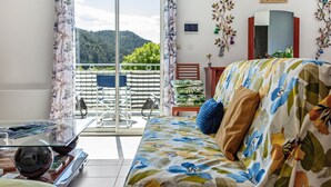 Ein Zimmer mit einer Couch, einem Glastisch, Blick auf einen Balkon mit einem Stuhl und einem dekorativen Spiegel.
