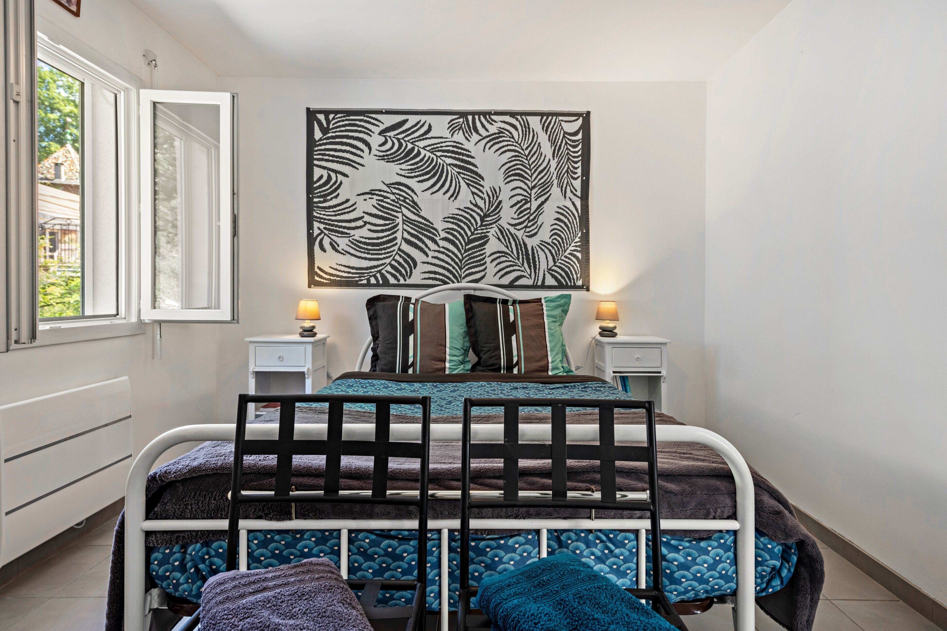 Une chambre à coucher comprenant un lit, deux tables de chevet, une œuvre d’art accrochée au mur et une fenêtre.