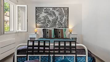 Une chambre à coucher comprenant un lit, deux tables de chevet, une œuvre d’art accrochée au mur et une fenêtre.