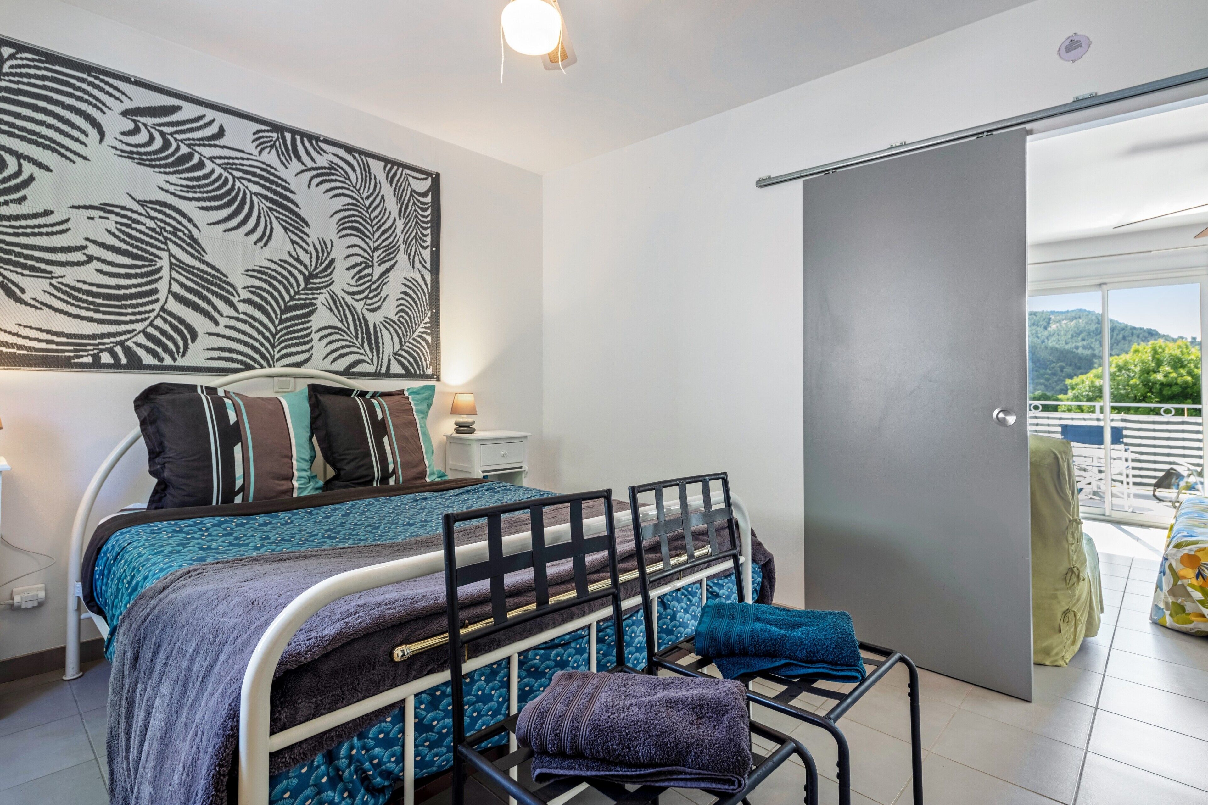 A bedroom with a bed, pillows, a nightstand, a wall art piece, and a door leading to an outdoor balcony.
