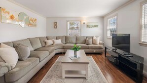 En stue med en hjørnesofa, et sofabord, et fladskærms-TV og kunst på væggene.