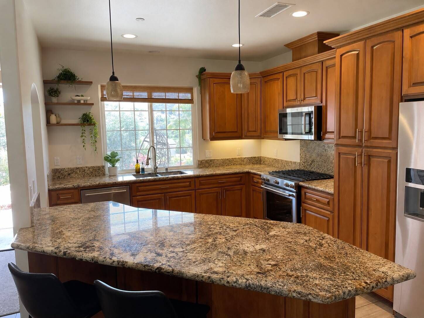A kitchen with wooden cabinets, granite countertops, a stainless steel refrigerator, and a built-in microwave.
