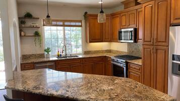 A kitchen with wooden cabinets, granite countertops, a stainless steel refrigerator, and a built-in microwave.