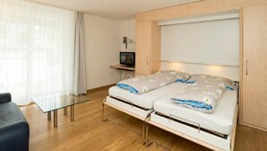 A bedroom with a bed, a TV, a glass table, and a wardrobe. - Chesa Quadrella by Interhome (Pontresina)