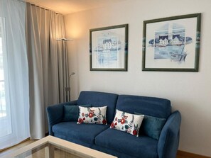 Ein blaues Sofa mit floralen Kissen, ein Glastisch und zwei gerahmte Kunstwerke an der Wand.