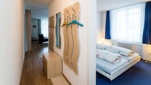 Ein Hotelzimmer mit Bett, einer kleinen Sitzecke, einem Flur und einer Wand mit abstrakter Kunst.