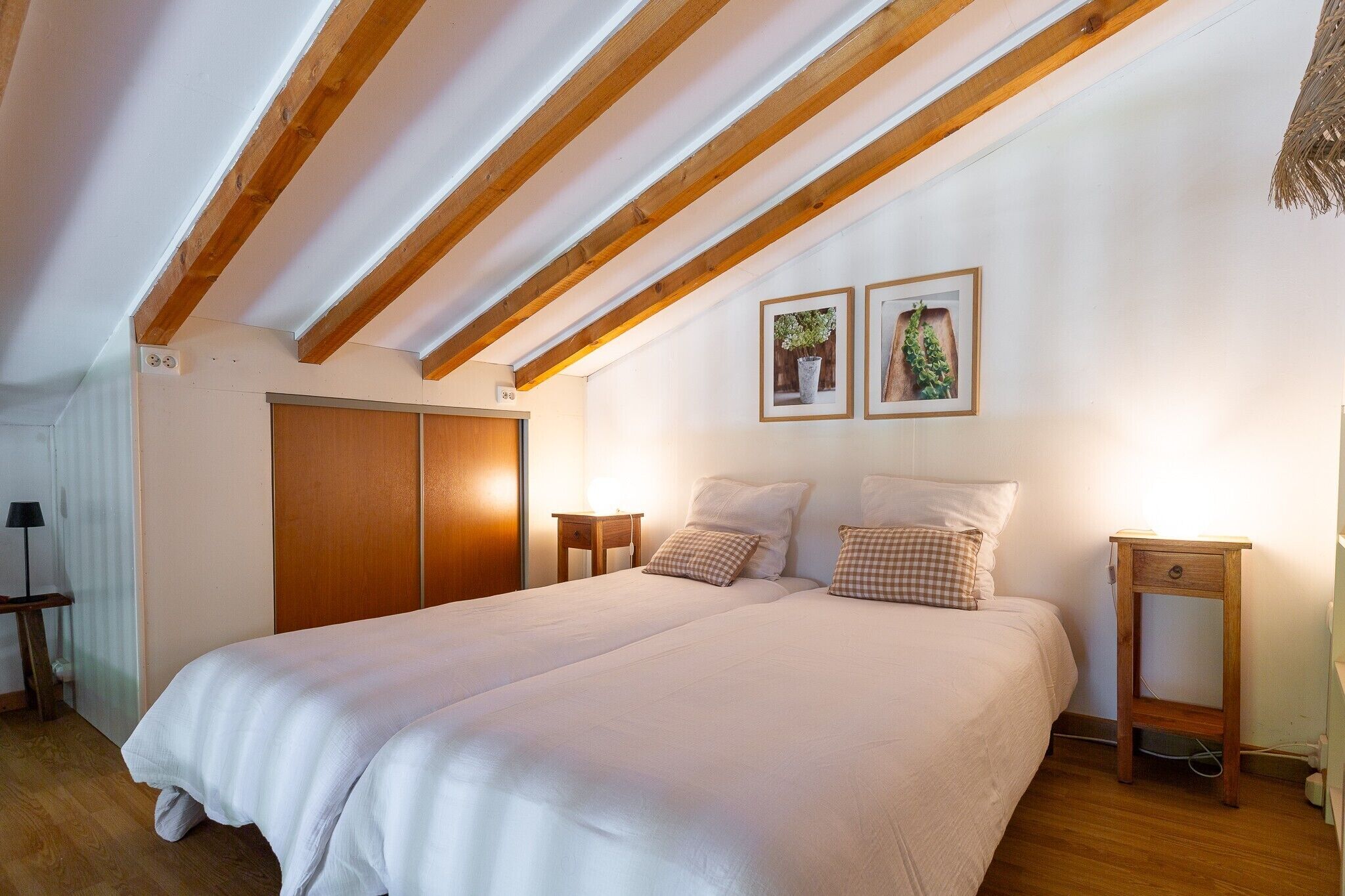 Une chambre avec un grand lit, des poutres apparentes, une armoire, des tables de chevet et deux tableaux encadrés au mur.