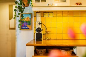 A kitchen with yellow tiles, a hanging basket, a framed picture, and a small appliance on the counter.