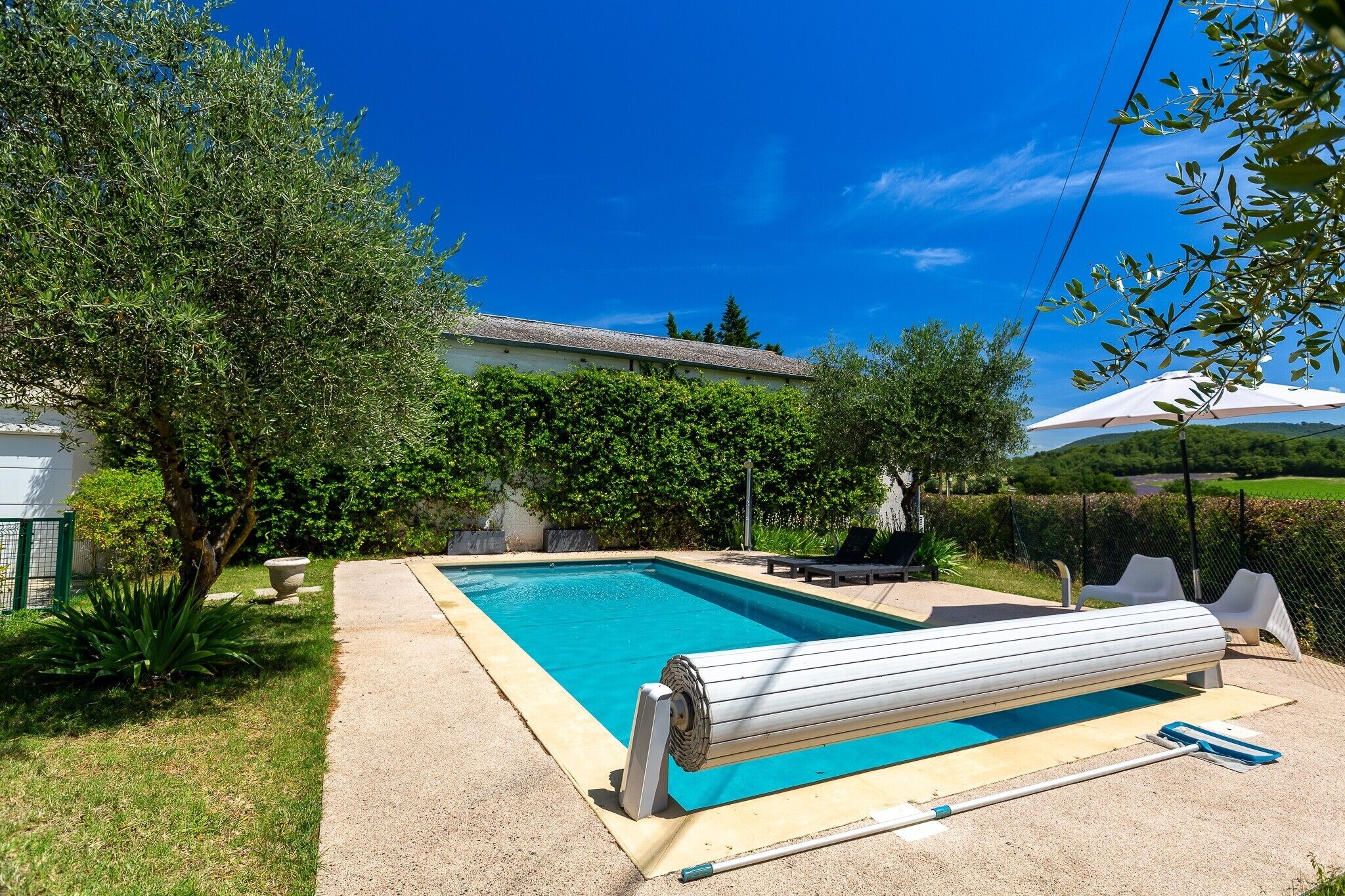 A rectangular swimming pool with a clear blue water surface, surrounded by a concrete deck and a grassy area.