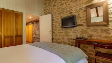 A bedroom with a bed, a television mounted on the wall, and a wooden wardrobe.