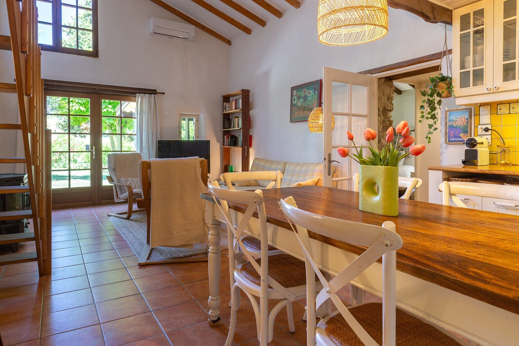 Un coin repas avec une table en bois, des chaises blanches et un vase rempli de fleurs.