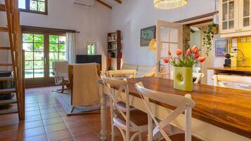 Un coin repas avec une table en bois, des chaises blanches et un vase rempli de fleurs.