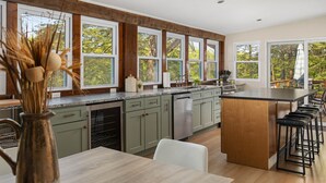 Una cocina moderna con una isla central, taburetes de bar y grandes ventanales que ofrecen vistas al exterior.