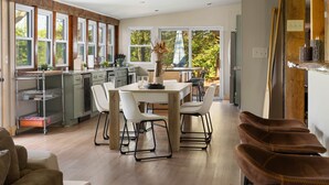 Una cocina moderna con comedor, ventanas amplias y vistas a árboles.