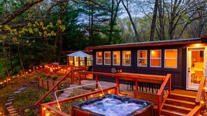 Una cabaña con jacuzzi, terraza de madera y luces colgantes.