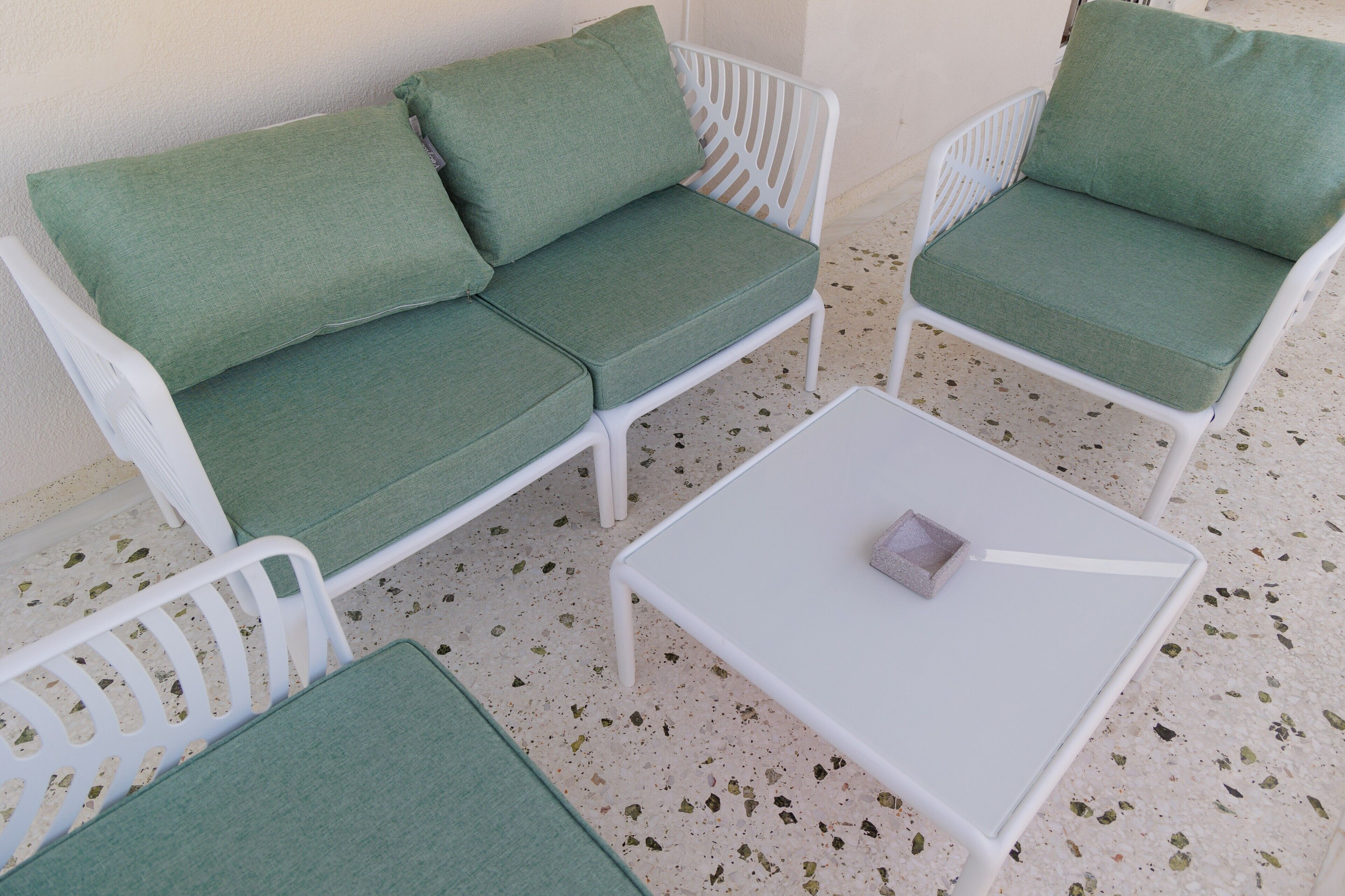 A white outdoor seating area with green cushions and a small table.