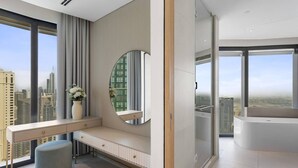 A modern bedroom with a large window, a round mirror, a bedside table, and a bench. - Exceptional high floor 3bed apartment by Suiteable (Dubai)