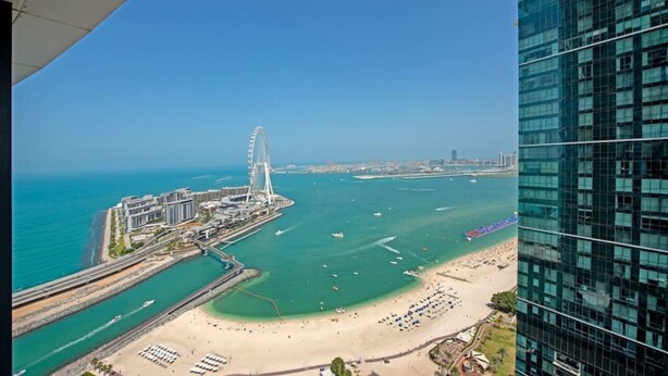 A coastal cityscape with a prominent Ferris wheel, a beach, and modern high-rise buildings. - Exceptional high floor 3bed apartment by Suiteable (Dubai)