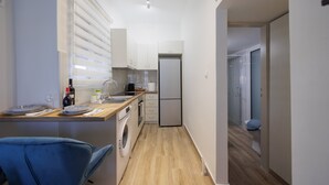Een compacte keuken met een wasmachine, een koelkast en een eethoek met een stoel.