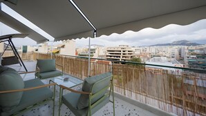 Een balkon met uitzicht op een stadsgezicht, een tafel en twee groene fauteuils met kussens.
