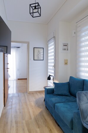 A living room with a blue sofa, a lamp, and a framed picture on the wall. - Cozy Studio with View in Athens – Private Terrace, Wi-Fi & Air Conditioning (Athina)